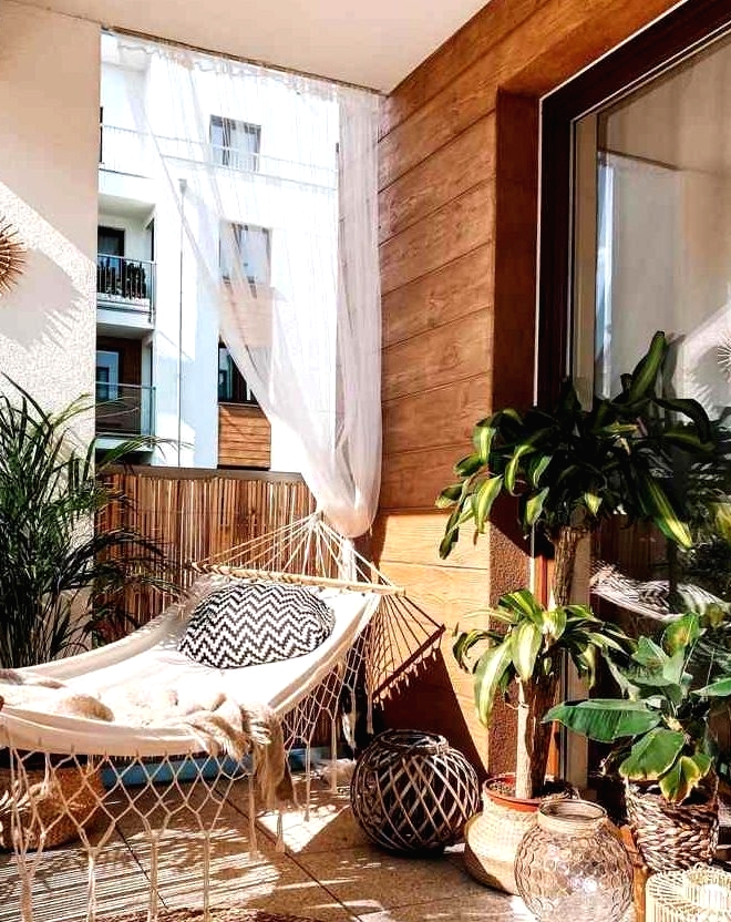 a boho balcony with a hammock and pillows, potted plants, candle lanterns, a jute rug and curtains, a sunburst mirror is a very cool and stylish idea to rock
