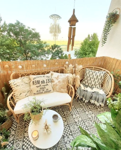 a cool boho balcony with black and white tiles, rattan furniture wiht boho pillows, potted plants and a round table with candles is cool