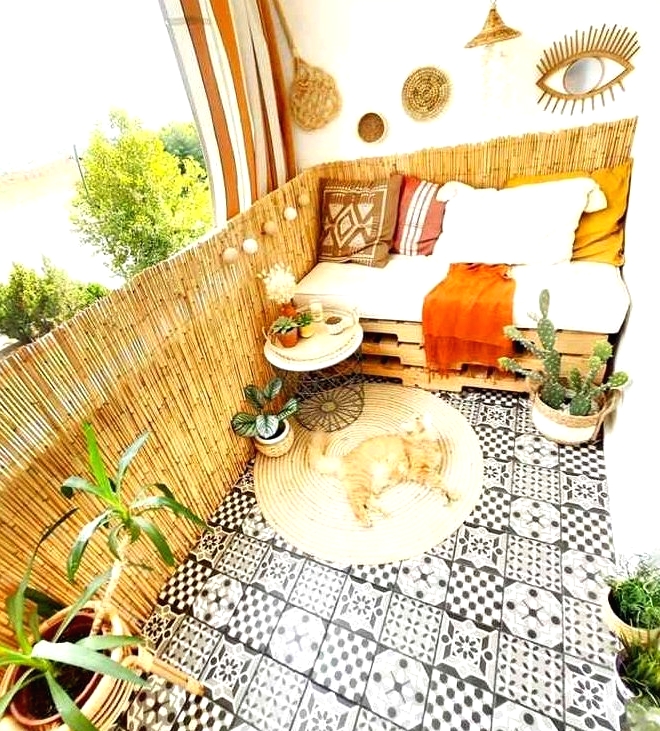 a pretty boho balcony with black and white tiles on the floor, a pallet seat with pillows, potted greenery, a jute rug and some baskets and lamps