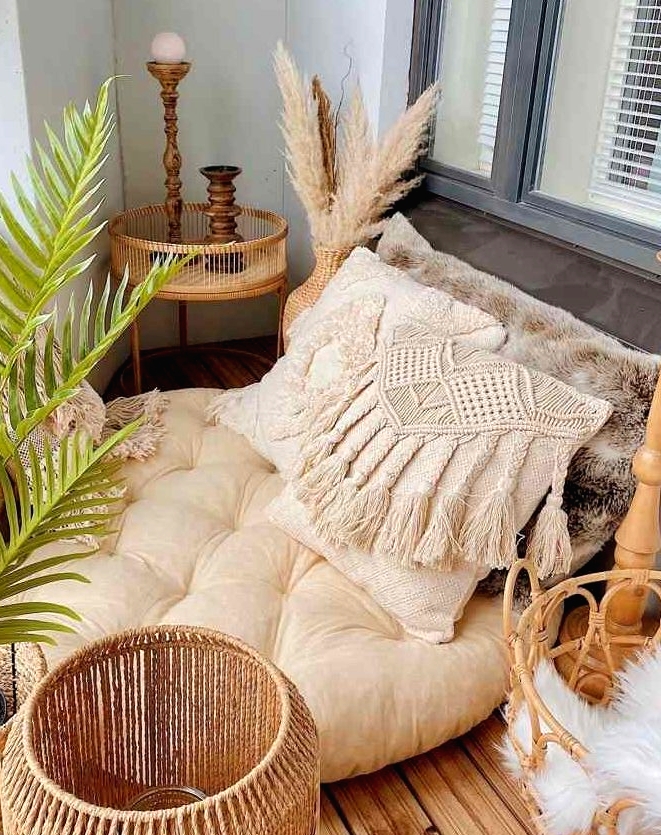 a tiny boho tropical balcony with a low seat with pillows, rattan baskets and a side table, candle lanterns, potted plants and pampas grass in a vase