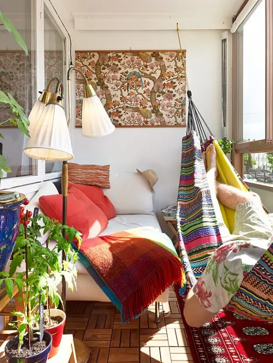 a mid-century modern meets boho balcony with a bright printed rug, a colorful boho hammock with pillows, a bold artwork and a neutral daybed with colorful pillows