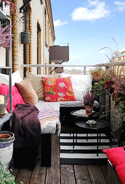 a bold boho balcony with a striped corner sofa with colorful pillows, lots of potted greenery and blooms around feels relaxed and free-spirited