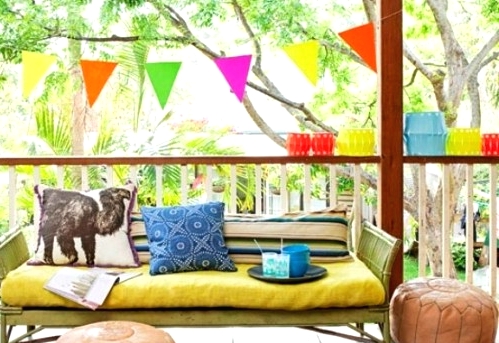 a super colorful balcony with a neon yellow loveseat, bold rugs and poufs, a colorful rug, colorful paper lanterns around