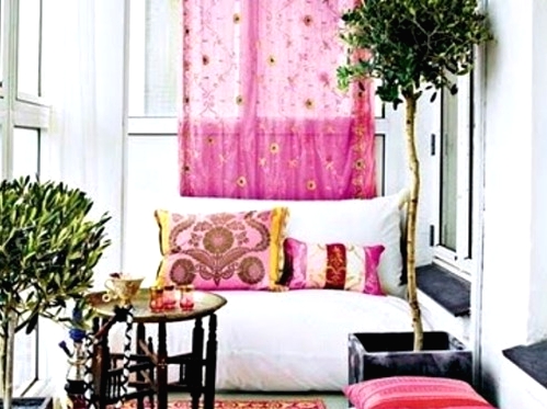 a boho colorful balcony with a bright rug, colorful pillows, a white loveseat, potted trees, a Moroccan side table and a view