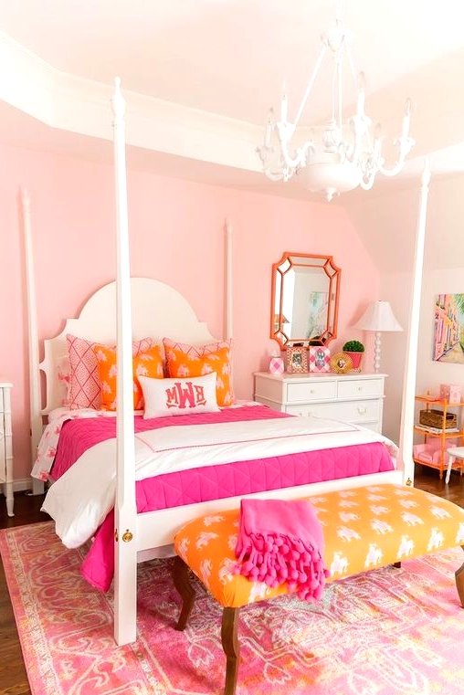 a bright pink girl's room with a vintage bed with colorful bedding, a yellow bench with a pink blanket, a white chandelier and a pink printed rug