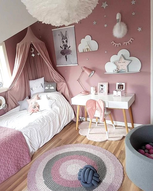 a dusty pink girl's bedroom, with a bed with dusty pink bedding and a canopy, a striped rug, a gallery wall and some star-shaped pillows