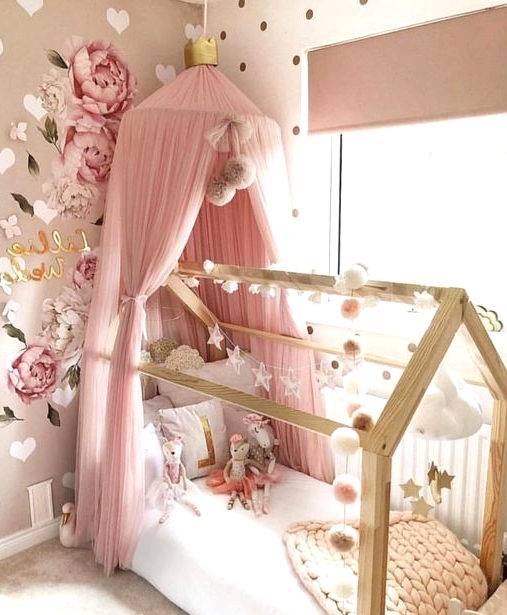 a gorgeous girl's bedroom with tan and white walls with hearts and polka dots, a bed with a pink canopy, garlands and paitned blooms