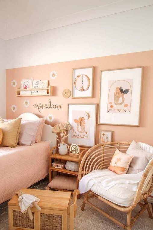 a lovely girl's room with a peachy accent wall and peachy bedding, stained and wicker furniture, a gallery wall and pillows