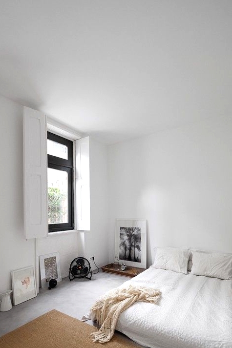 a minimalist neutral bedroom with a low bed with white bedding, a tan jute rug, some art and other stuff right on the wall