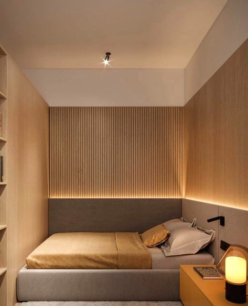 a small and minimal bedroom with wooden slab walls and built-in storage units, an upholstered bed and a long nightstand plus built-in lights