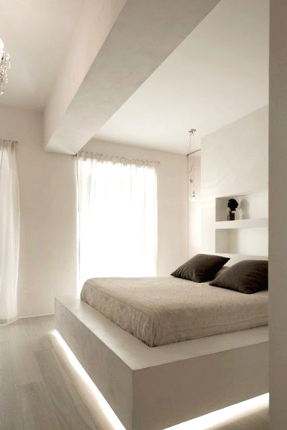 a white ultra-minimalist bedroom with a floating slab bed with lighting, niches for storage, a crystal chandelier for an elegant touch