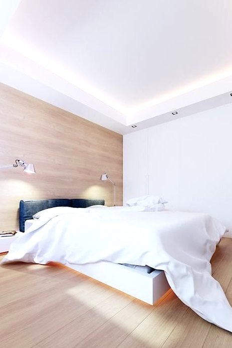 a stylish minimalist bedroom with a white raised bed with lights, an upholstered headboard, some lamps and a large sleek storage unit