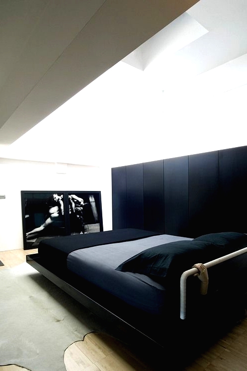 a minimalist bedroom with a sleek black storage unit, a glossy black bed with grey and black bedding, a statement artwork and a grey rug plus lots of natural light