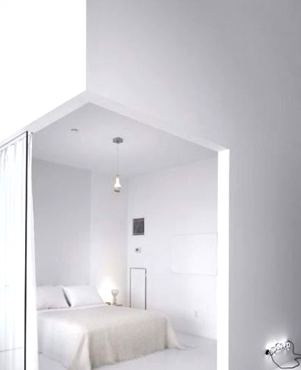 a crispy white minimalist bedroom with a white bed and bedding, pendant and table lamps and a glass space divider with curtains