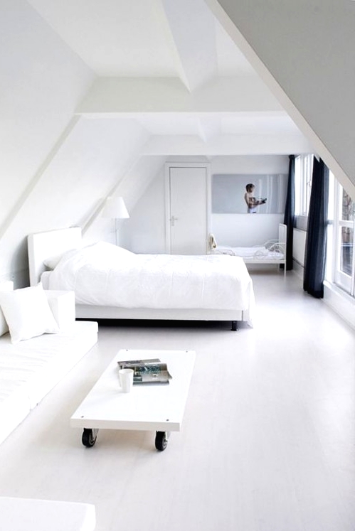 a minimalist white bedroom with a white bed, a white corner sofa, a coffee table on casters and a smaller bed for a kid is cool