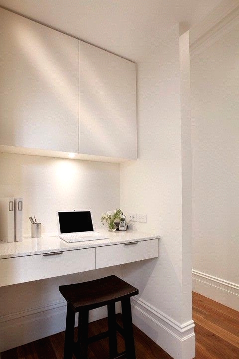 a sleek white working space with a large sleek cabient for storage, a built-in desk, a dark stool and some built-in lights