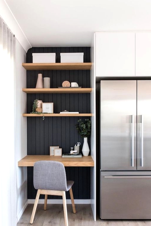 a small awkward nook with black shiplap, built-in shelves and a desk, a comfy grye chair for working in the kitchen