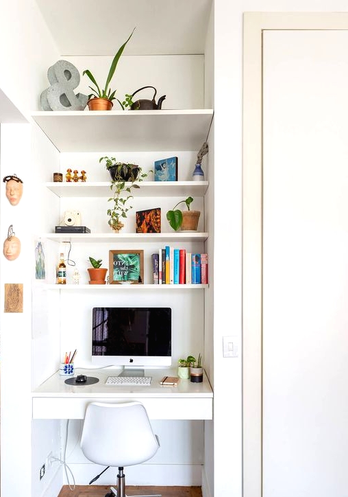 a tiny nook with built-in shelves and a desk with a drawer, a white chair, books and potted plants is a cool space fo working