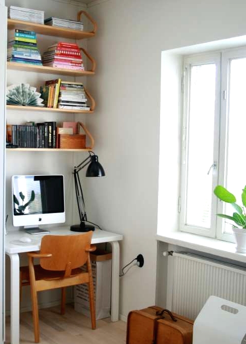 a small nook by the window with a white desk and some suspended shelves, a plywood chair and a black table lamp