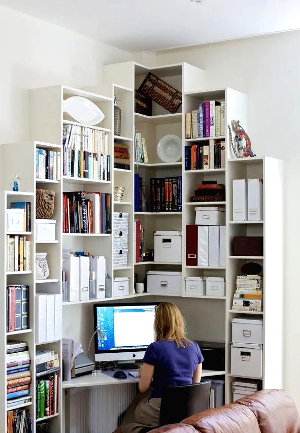 an awakward corner turned into a working space with a large shelving unit that includes a triangle desk and a black leather chair