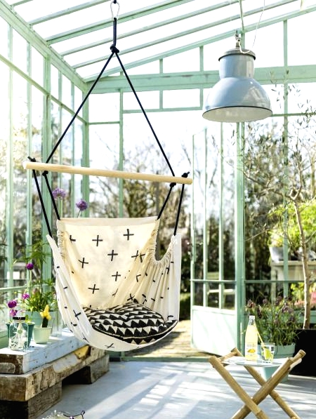 a lovely sunroom or glass house with a pendant chair, some stools, a reclaimed wooden bench with potted blooms is cool