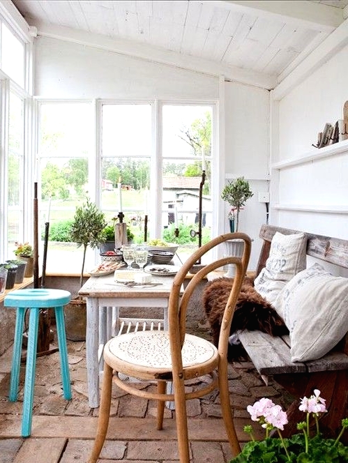 a Nordic sunroom with a shabby chic bench, a whitewashed table, mismatching chairs and stools and potted greenery