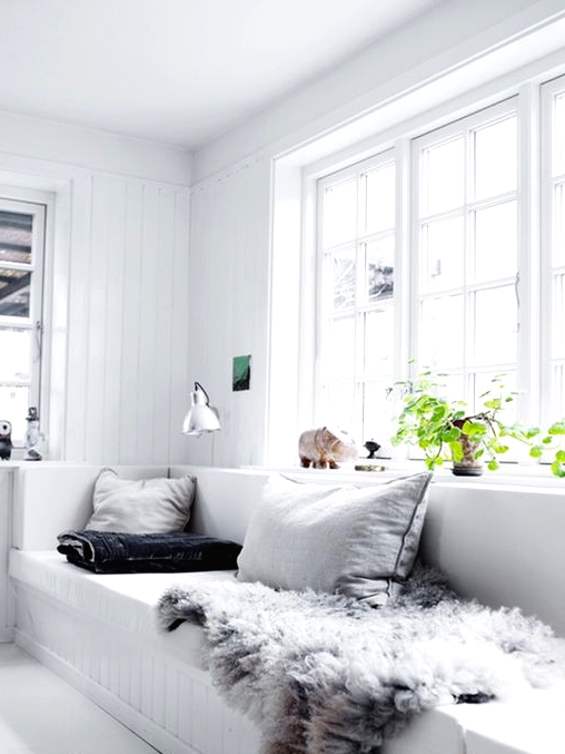 a relaxed white Scandinavian sunroom with a built-in sofa, neutral pillows, a sconce and a potted plant is all cool