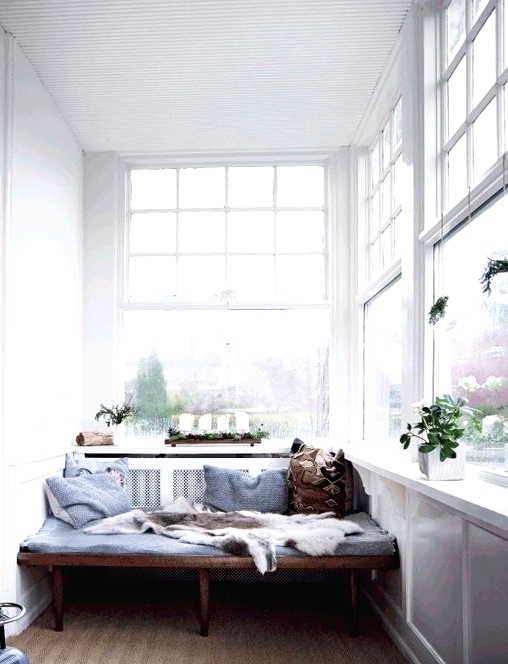 a Scandinavian sunroom with a built-in stained bench, blue bedding, potted plants and a printed rug is a lovely space