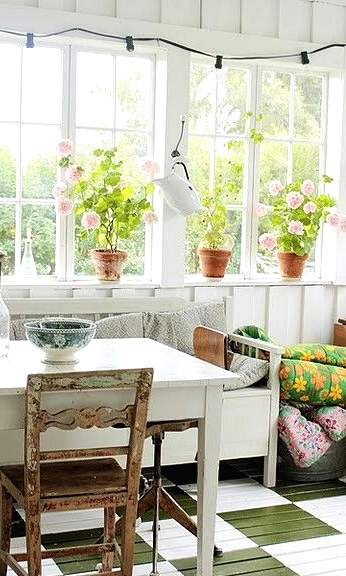 a vintage Nordic sunroom with a checked green and white floor, vintage white and stained furniture, colorful blankets and potted blooms
