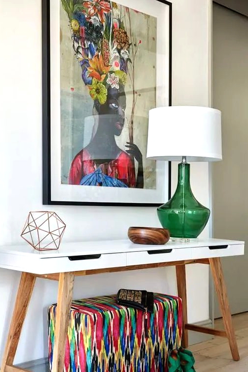a chic white mid-century modern console table with a super colorful artwork, a bright upholstered ottoman and a green lamp for summer