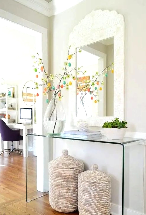 a clear glass console table, baskets with jars, books, succulents, an Easter tree in a large vase and a mirror in an ornated frame