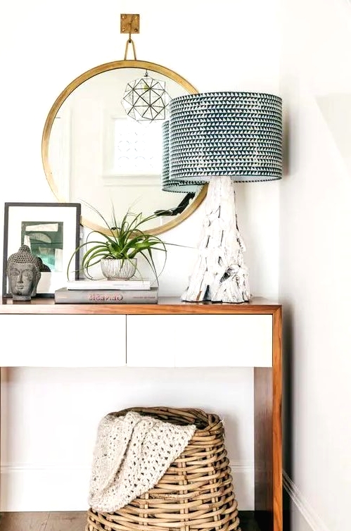 a small mid-century modern console table, a brass frame mirror, a lamp with a driftwood base, a potted plant, some art and a basket