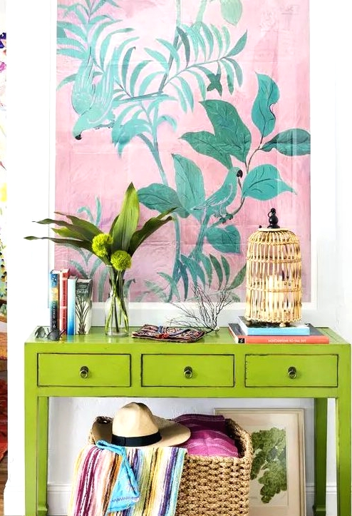 a super bright neon green console with a birdcage candle holder, greenery, a bold artwork and a basket with colorful textiles