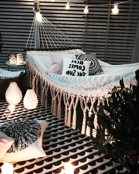 a black and white outdoor nook with a hammock, printed pillows, baskets with greenery, candles and candle lanterns