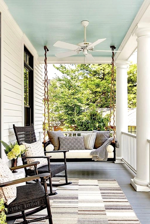 a chic vintage-inspired black and white porch with a black hanging bench with neutral upholstery, black wicker rockers and printed pillows