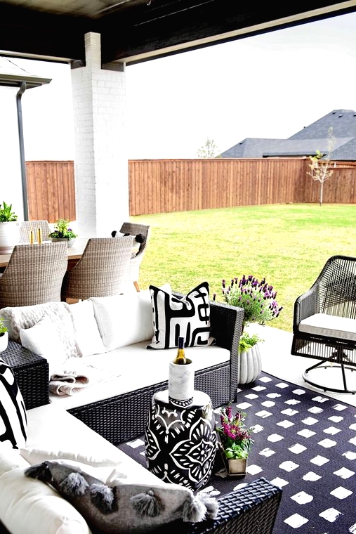 a patio with black wicker chair and black and white upholstery and a black and white printed stool plus blooms