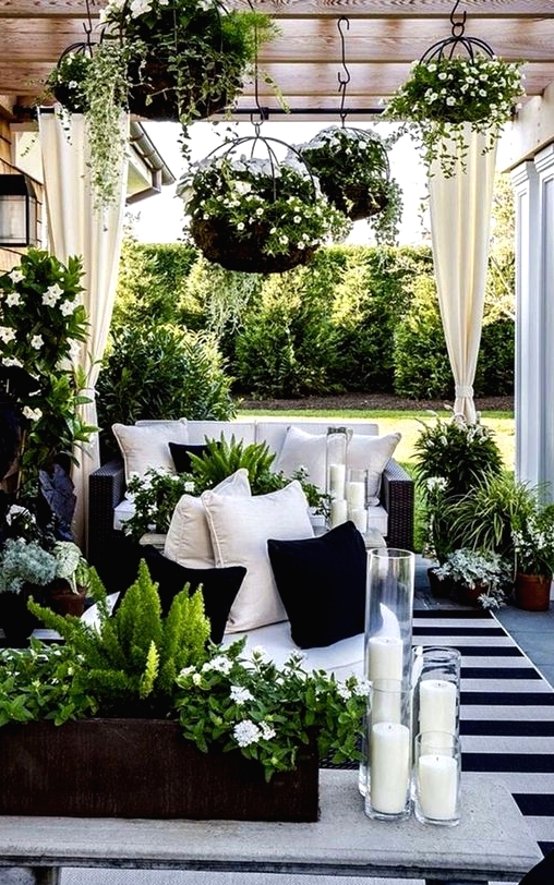 a stunning black and white terrace with black wicker furniture, a stone bench, lots of greenery, blooms and candles