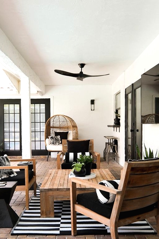 a stylish terrace with a brick floor, stained furniture, black and white upholstery, potted greenery and a low coffee table