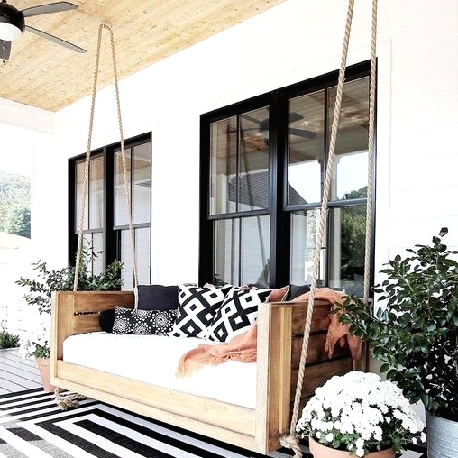 a terrace with a black and white rug, a hanging bench and printed pillows and potted greenery and blooms