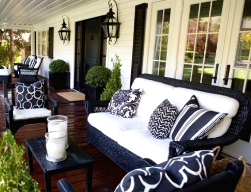 a farmhouse porch with black and white wicker furniture, printed pillows, potted greenery and pillar candles