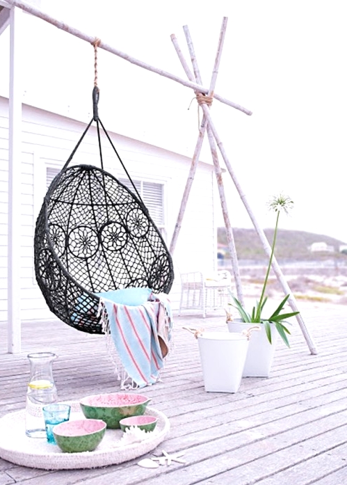 a relaxed tropical whitewashed deck with a black woven pendant chair, blooms in pots is a very cool and fresh idea