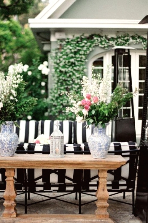 an elegant outdoor space with a striped sofa, a rustic wooden console table and lots of fresh blooms and greenery