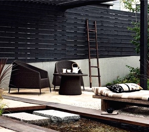 a stylish modern outdoor space with dark wicker chairs, a wooden daybed, printed pillows and a blanket