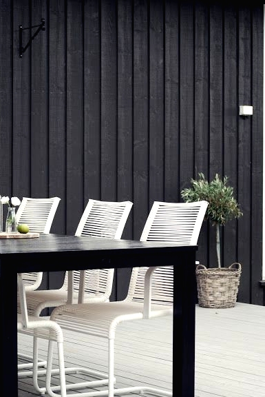 a minimalist outdoor dining space with a black dining table, white metal chairs, a potted tree and some greenery is chic