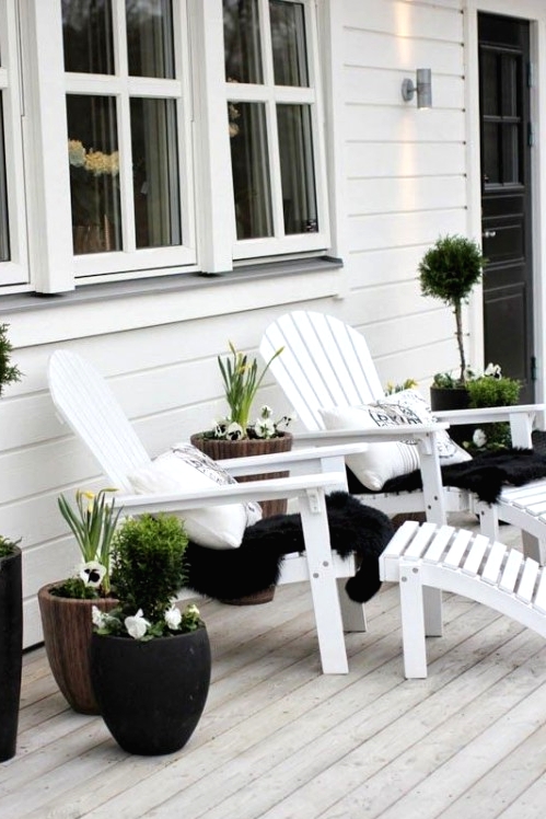 a white deck accented wiht black touches, with white loungers, black blankets and potted plants in black pots for a contrast