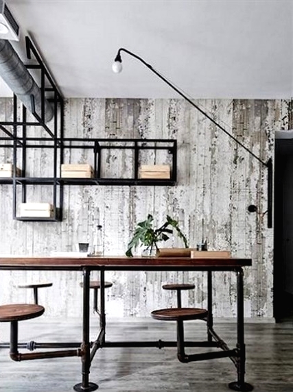a rustic industrial home office with a large wooden desk and stools attached, exposed piping and a shelving unit