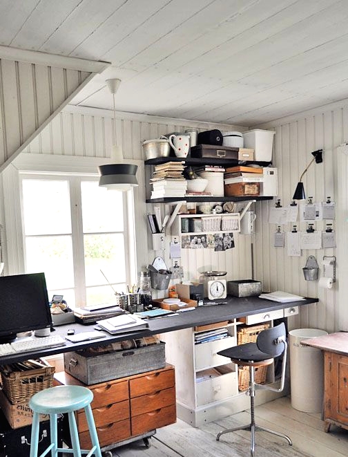 an industrial home office with shiplap walls and a whitewashed floor, a shared desk with mismatching stools and black shelves