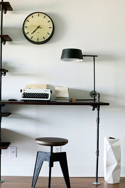 a small industrial working space of a wood and metal shelving unit that includes a desk and a matching stool plus a black table lamp