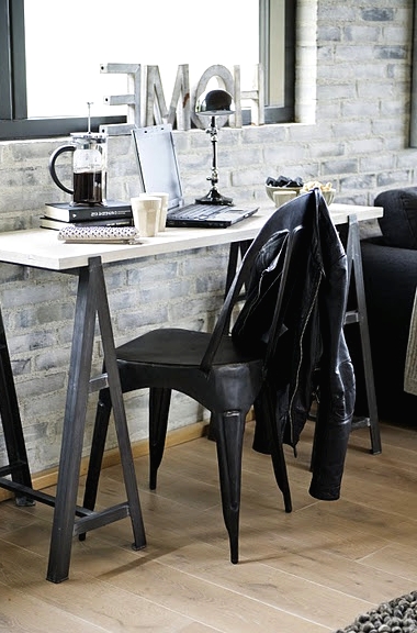 an industrial home office with white brick walls, a trestle desk, a black chair and some pretty decor