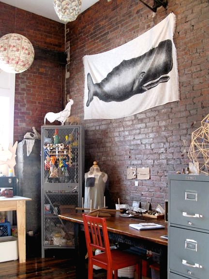 an industrial home office with red brick walls, metal storage units, a wooden desk and a red chair, paper pendant lamps